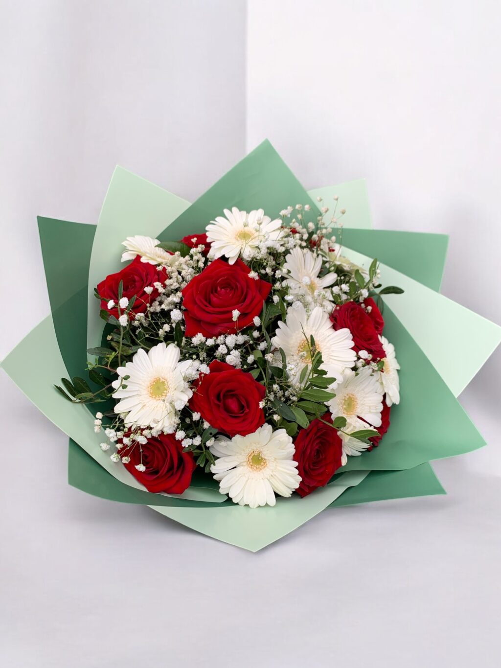 Strauß aus roten Rosen, weißen Gerbera und Schleierkraut.